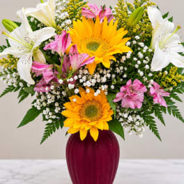 Bouquet of sunflowers, lilies, and pink alstroemeria in a burgundy vase