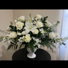 White roses and lilies arranged in a white urn vase
