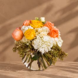 Bouquet of yellow, peach, and white flowers in a clear glass vase