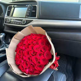Bouquet of red roses wrapped in beige paper on a car seat