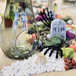 Glass vase with Halloween graveyard decorations and white pebbles