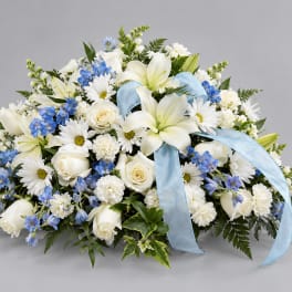 White lilies, roses, and blue flowers arranged with a light blue ribbon