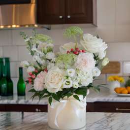 White and blush floral arrangement in a round box with a ribbon