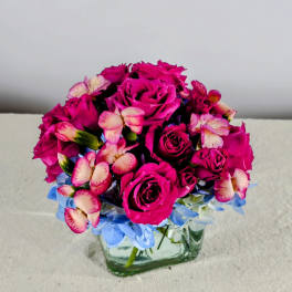 Pink rose bouquet in a square glass vase with blue flowers