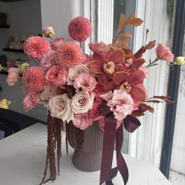 Pink and peach floral arrangement in a ribbed vase with a ribbon bow