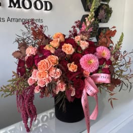 Large mixed bouquet of pink, peach, and burgundy flowers in a black hatbox with a pink ribbon.