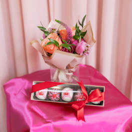 Pink and peach bouquet in a glass vase with a box of chocolates
