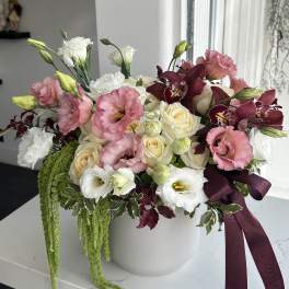 Pink and white floral arrangement in a white vase with a burgundy ribbon