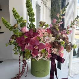 Pink and cream floral arrangement in a green box with a purple ribbon