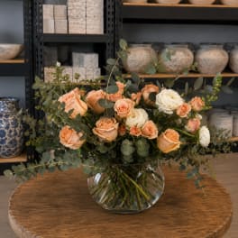 Peach and white roses in a clear glass vase with eucalyptus