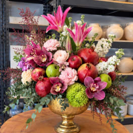 Mixed floral arrangement with orchids, apples, and pomegranates in a gold vase