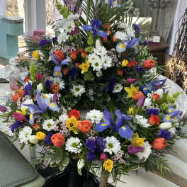 Colorful spring wreath and matching arrangement with irises, tulips, daffodils, and daisies in a circular design.