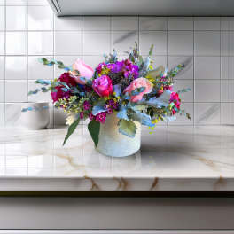 Mixed pink and purple flower arrangement in a white vase