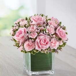 Pink roses and carnations arranged in a square glass vase
