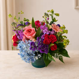Mixed bouquet of roses, hydrangeas, and purple blooms in a glass vase