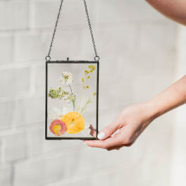 Pressed flowers in a hanging glass frame held by two hands