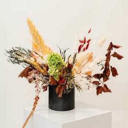Dried floral arrangement in a black vase with green hydrangea and tan, white, and red accents