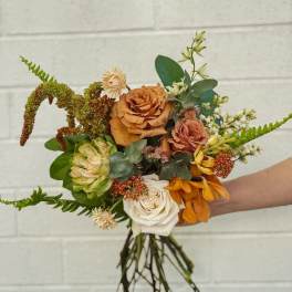 Handheld bouquet of orange, white, and green flowers