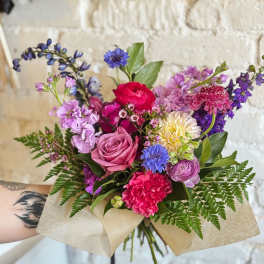 Hand-tied bouquet of pink, purple, and blue flowers wrapped in paper