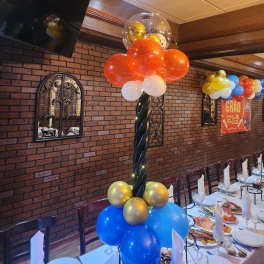 Balloon centerpiece with orange, blue, gold, and white balloons at a decorated table.