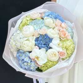 Pastel bouquet of hydrangeas, roses, and white orchids wrapped in pink paper