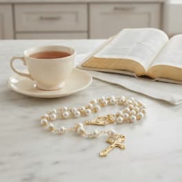 Pearl rosary beside a teacup and open book on a marble surface