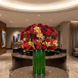 Large red and gold floral arrangement in a tall green glass vase