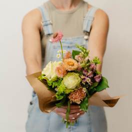 Handheld bouquet of mixed pastel flowers wrapped in brown paper