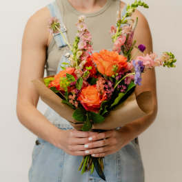 Person holding a colorful mixed bouquet wrapped in brown paper