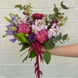 Handheld bouquet of pink and purple flowers with greenery