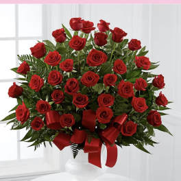 Large arrangement of red roses with red ribbon in a white pedestal vase