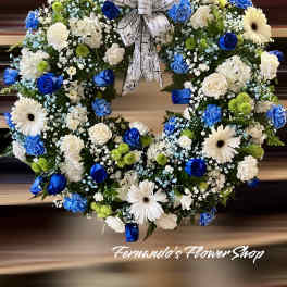Round wreath of blue and white flowers with green accents and a printed memorial ribbon bow
