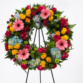Colorful floral wreath on a black stand with roses, gerbera daisies, and hydrangeas