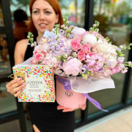 Pink and lavender flower arrangement in a round box with a chocolate gift box