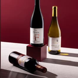 Three wine bottles arranged on a burgundy and white surface