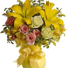 Yellow lilies and pink roses in a yellow vase with a ribbon