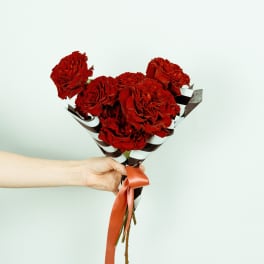 Handheld bouquet of red roses wrapped in striped paper with a ribbon