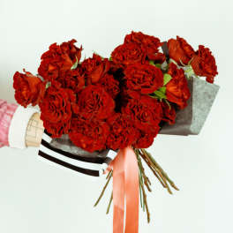 Bouquet of red roses wrapped in dark paper with a pink ribbon