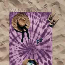 Purple tie-dye beach blanket with a straw hat, sandals, sunglasses, and a tote bag