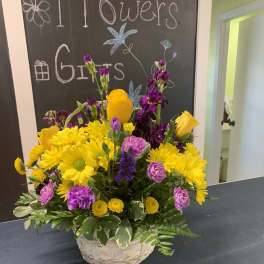 Basket arrangement of yellow daisies, purple flowers, and yellow roses