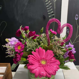 Pink gerbera daisies and mixed flowers in a striped vase with a heart pick
