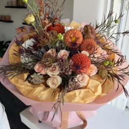 Bouquet of peach, orange, and cream flowers wrapped in pink paper