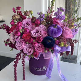 Pink and purple floral arrangement in a purple hat box with ribbon