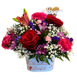 Mixed bouquet of red roses, lilies, and pink carnations in a decorated container