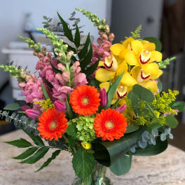 Mixed bouquet with yellow orchids, orange gerbera daisies, and pink snapdragons in a glass vase
