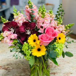 Mixed bouquet with pink roses, yellow daisies, and dark orchids in a glass vase