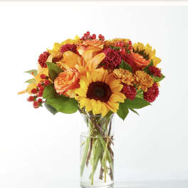 Bouquet of sunflowers, orange roses, and red mums in a clear glass vase