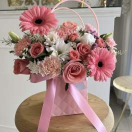 Pink and white flower arrangement in a pink gift bag with ribbon handles