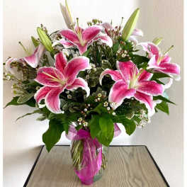Pink stargazer lilies arranged in a clear vase with a pink ribbon.