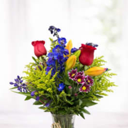 Mixed bouquet of roses, lilies, and blue flowers in a glass vase